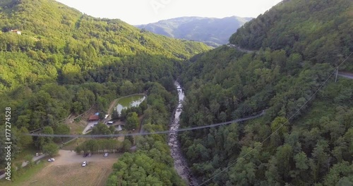 Aerial, suspended bridge in the wood with some tourist on it and a mountain river under in San Marcello Pistoiese in Tuscany, Italy photo