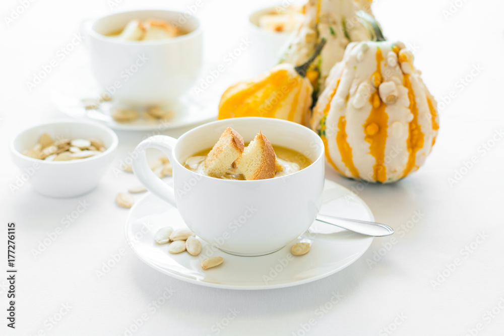 Two cups with fresh pumpkin cream soup decorated cream, seeds and crackers on white table cloth Two cups with fresh pumpkin cream soup decorated cream, seeds and crackers on white table cloth
