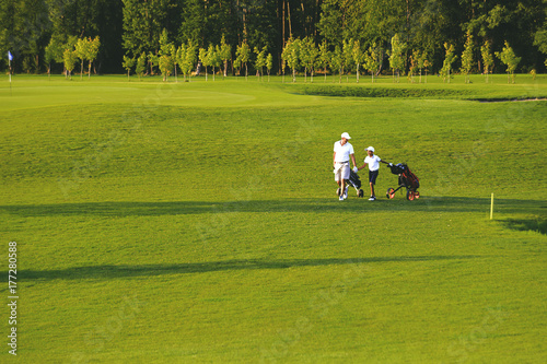 man with his son golfers walking on perfect golf course at summer evening