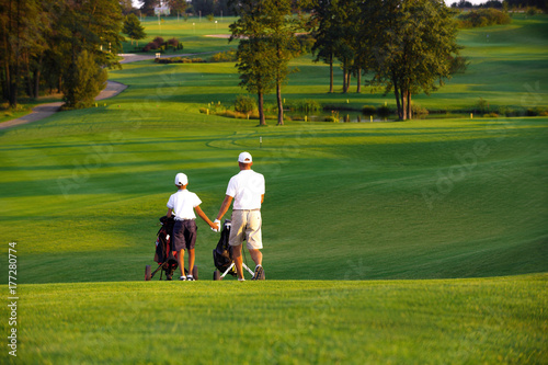 man with his son golfers walking on perfect golf course at summer evening
