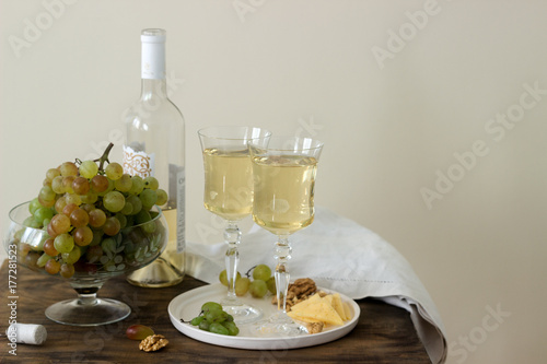 Glasses with white wine and a bottle of wine with a snack - cheese, walnuts and grapes. Rustic style.