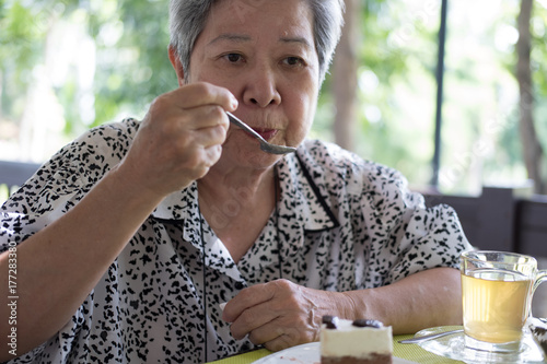 elder senoir eating chocolate mousse cake at cafe. elderly woman sitting and tasting delicious dessert at restaurant. photo