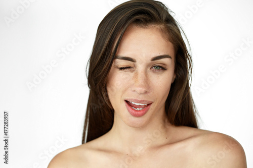 Pretty young woman gives a wink standing on white background