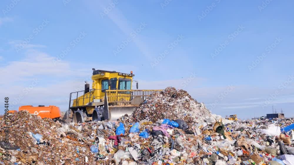 A landfill compactor bulldozer levels down a pile of trash. Water, air contamination concept.