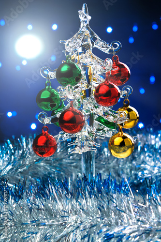 Glass christmas tree with colorful balls on blurred lights background