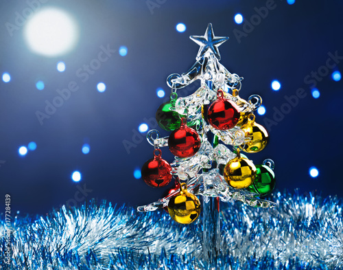 Glass christmas tree with colorful balls on blurred lights background