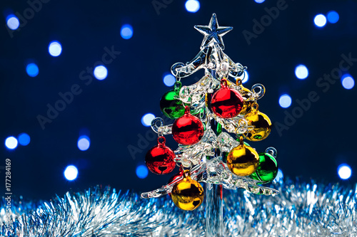 Glass christmas tree with colorful balls on blurred lights background