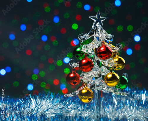 Glass christmas tree with colorful balls on blurred colored lights background