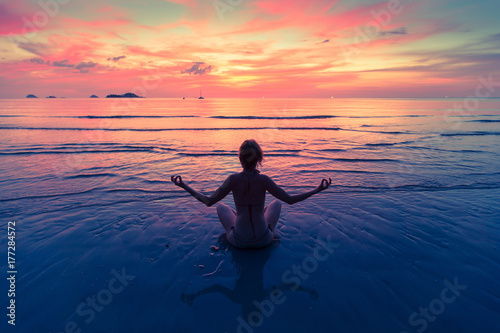 Young woman practicing yoga sitting on the sea beach during an amazing sunset. © De Visu