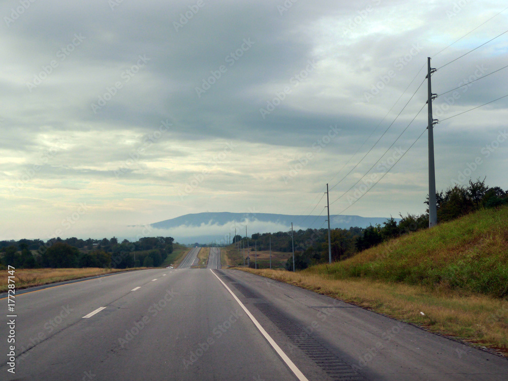 Open road with mountains in the distance, electric lines, fog and mist and clouds