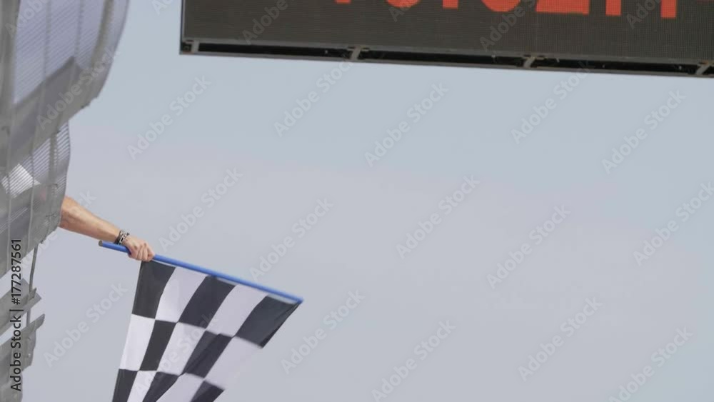 Man holding and waving Checkered race flag in slow motion at finish line on a raceway. Victory, achievement, success and sport concept.