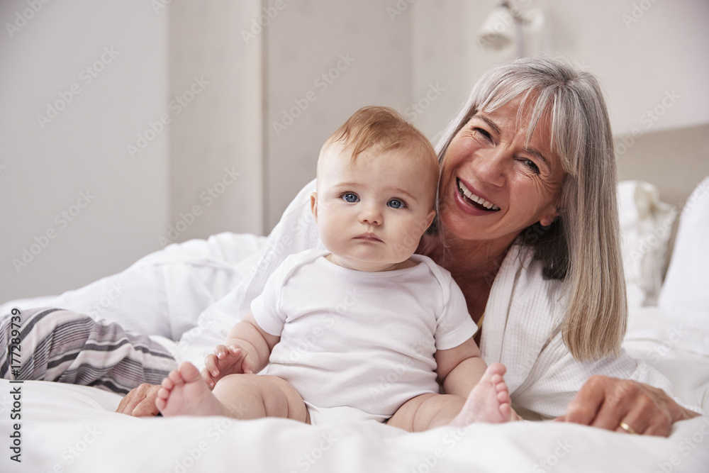 Grandmother Lying In Bed At Home Looking After Baby Grandson Grandmother Lying In Bed At Home Looking After Baby Grandson