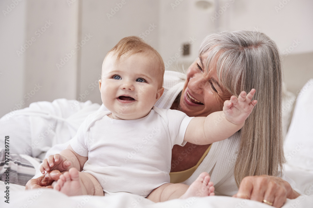 Grandmother Lying In Bed At Home Looking After Baby Grandson Grandmother Lying In Bed At Home Looking After Baby Grandson
