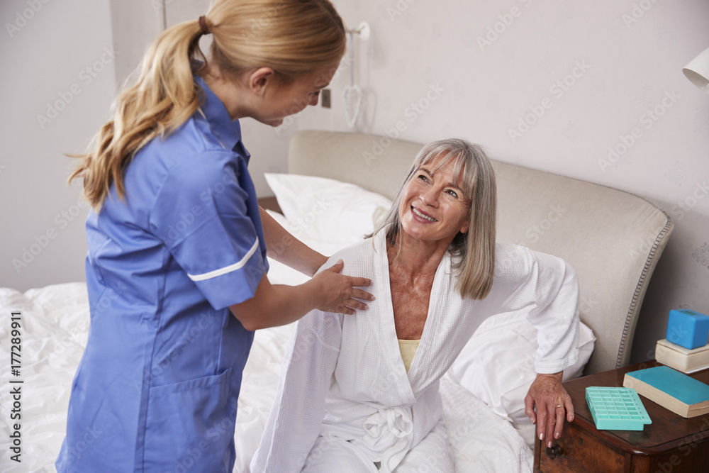 Fototapeta premium Nurse Helping Senior Woman Out Of Bed On Home Visit