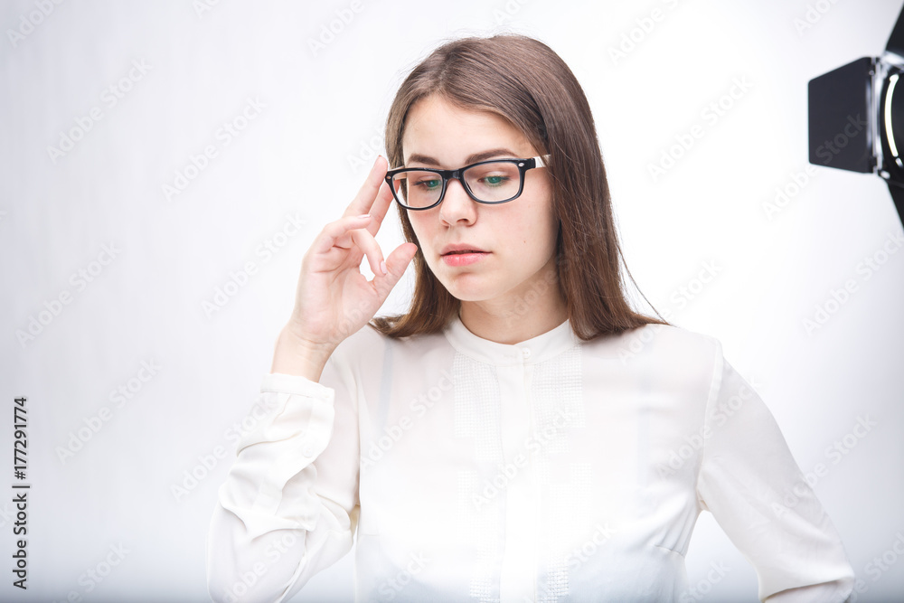 beautiful young girl in glasses with black frame, with brown hair over shoulders and white shirt on white isolated background.