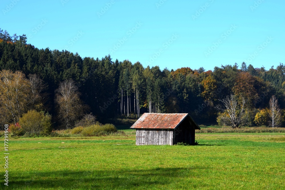 Herbstliche Landschaft mit alter Holzhütte und verfärbten Mischwald in Bayern