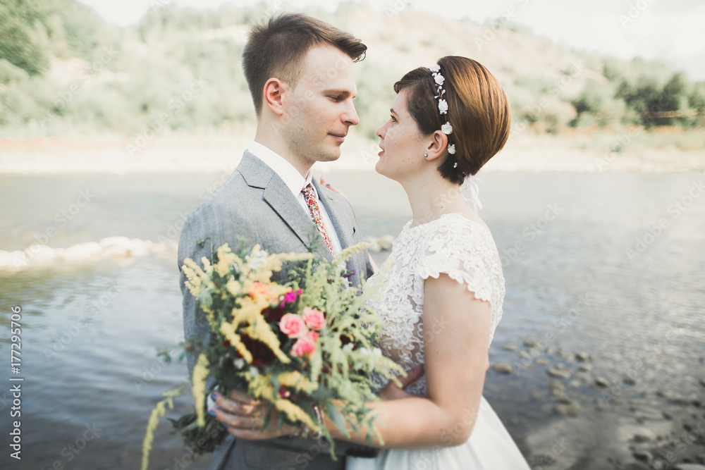 Beautifull wedding couple kissing and embracing near the shore of a mountain river with stones Beautifull wedding couple kissing and embracing near the shore of a mountain river with stones