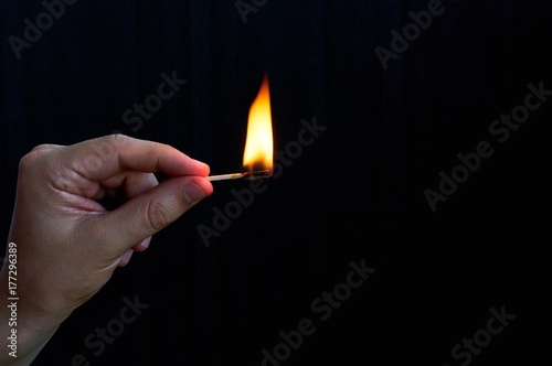 Hand holding burning match stick on black background