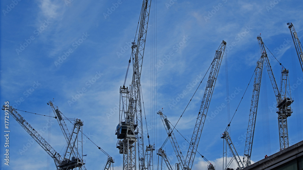 Tower cranes on a UK construction site viewed against a blue autumnal sky