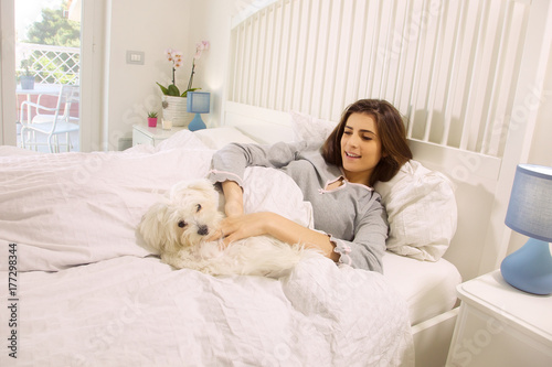 cute woman playing with dog in bed at home