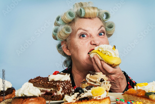 Senior Woman with Rollers in her Hair, indulging in her Guilty pleasure of eating too many cakes / Sweets photo