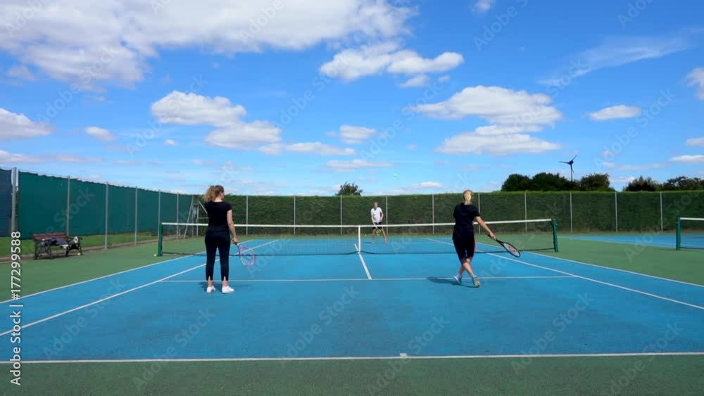 Slow motion shot of two pretty young women and a handsome man in their twenties, playing tennis on a court outdoors. Slow motion shot of two pretty young women and a handsome man in their twenties, playing tennis on a court outdoors.