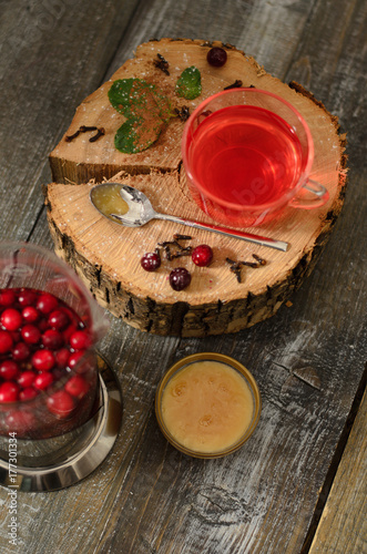 Hot drink of cranberries in а teapot and in a cup with honey on wooden background