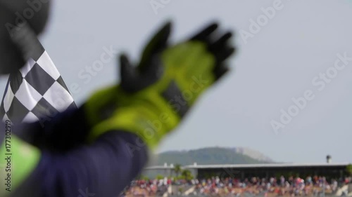 Man holding and waving Checkered race flag in slow motion at finish line on a raceway. Hands of unidentified person applauding.Victory, achievement, success and sport concept.