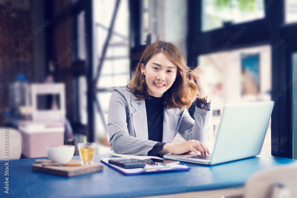 Smiling beautiful Asian girl with black hair working in cafe,Casual woman manager sitting in her office workspace with computer and big bright window and drinking coffee ,look at camera,vintage color Smiling beautiful Asian girl with black hair working in cafe,Casual woman manager sitting in her office workspace with computer and big bright window and drinking coffee ,look at camera,vintage color
