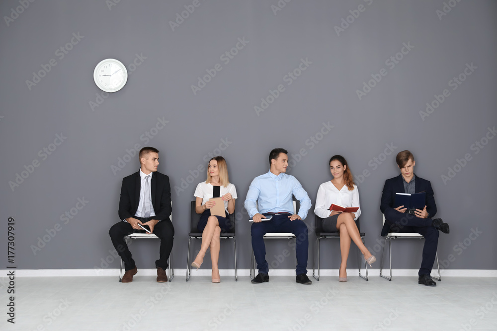 Group of people waiting for job interview on gray wall background