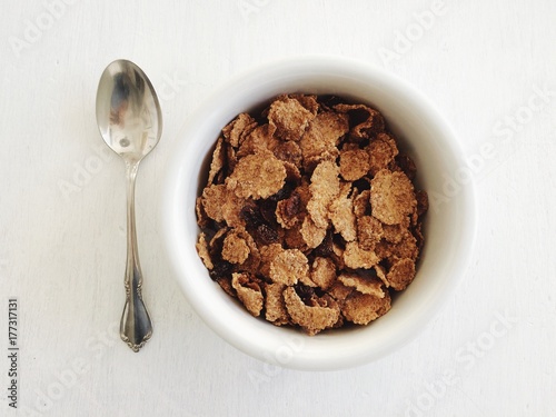 A bowl of fresh breakfast cereal on a white table with a silver spoon