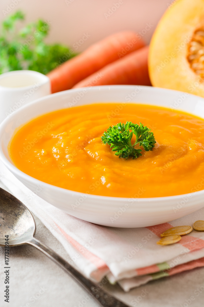 Pumpkin and carrot cream soup with parsley on gray stone background. Pumpkin and carrot cream soup with parsley on gray stone background.