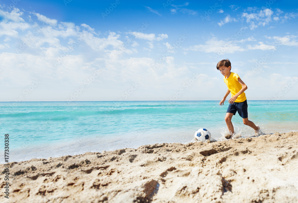 Portrait of cute boy playing football on beach