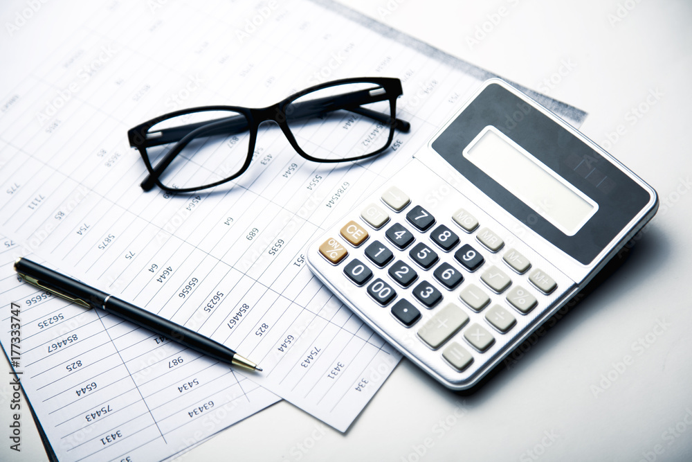 Glasses and calculator on paper table with finance report Glasses and calculator on paper table with finance report