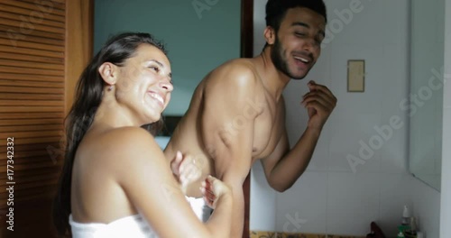 Couple In Bathroom Woman Washing Face Talking To Man In Towels Doing Morning Routine Hygiene Looking In Mirror