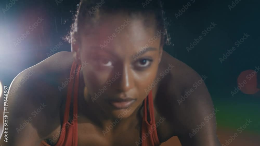  Female runner at athletics track crouching at starting blocks before a race