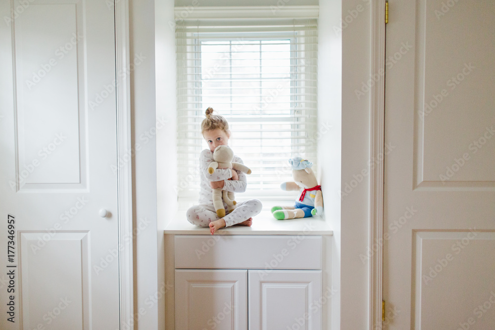 little girl sitting in a window seat and hugging a stuffed animal little girl sitting in a window seat and hugging a stuffed animal