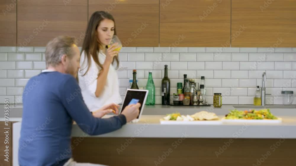 Cheerful couple chatting in the kitchen of modern home, man shopping online Cheerful couple chatting in the kitchen of modern home, man shopping online