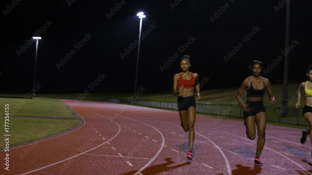  Competitive female athletes running at race track in the dark. Slow motion.