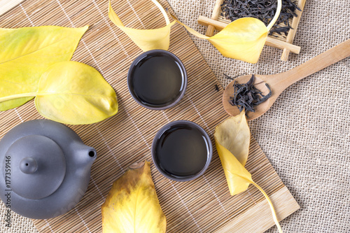 Black teapot and cups with yellow leaves on the table. Hot drinks. Autumn tea. Top view.