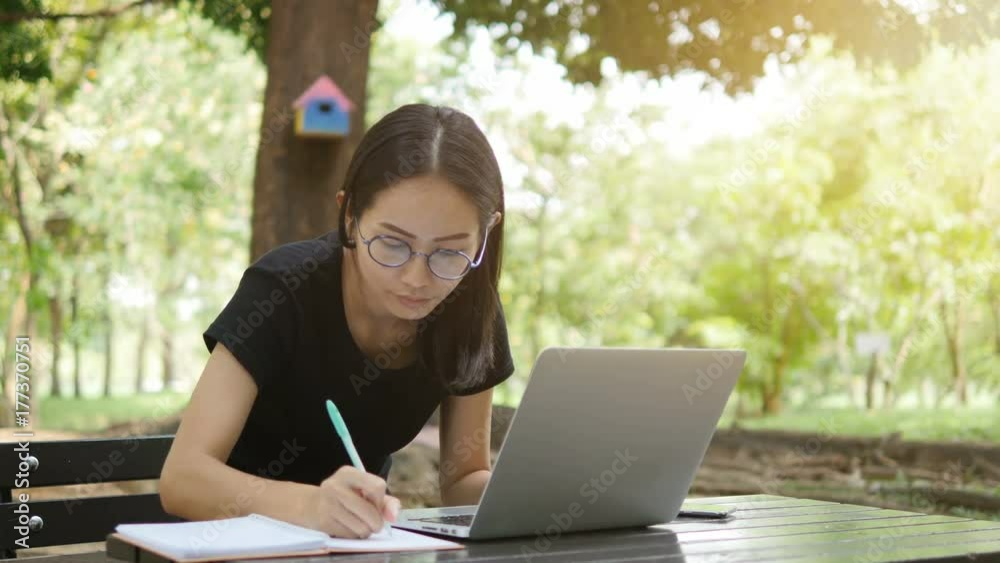 4K: Asian woman working on modern laptop in the park. 4K: Asian woman working on modern laptop in the park.