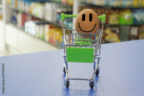 Egg happily smiling inside a mini trolley with blurred background of shop interior. Conceptual photo