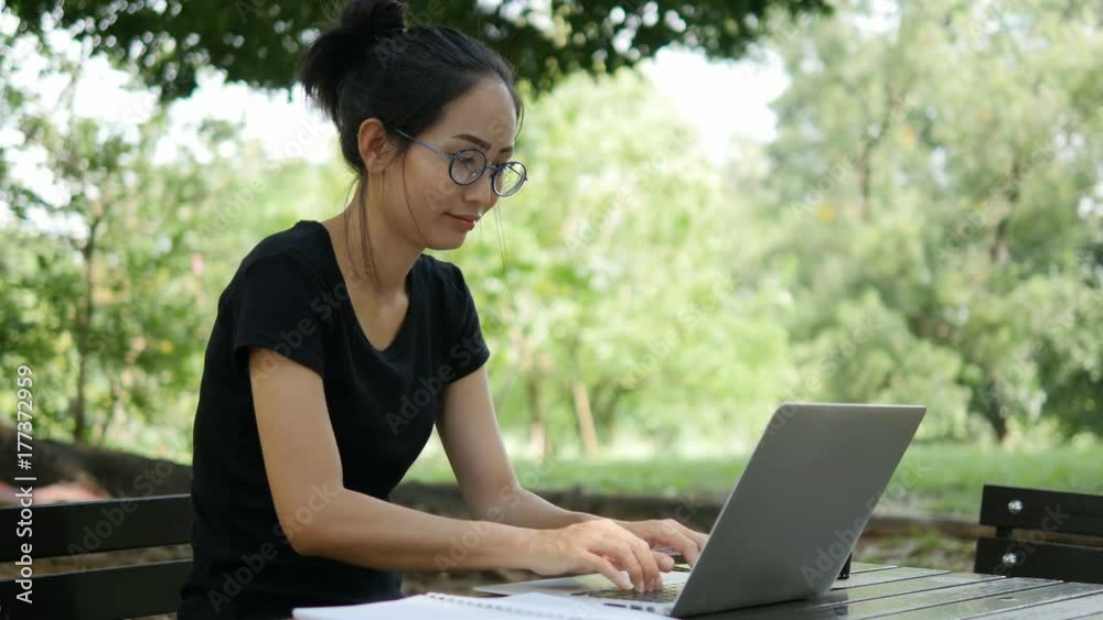 4K: Asian woman working on modern laptop in the park. 4K: Asian woman working on modern laptop in the park.