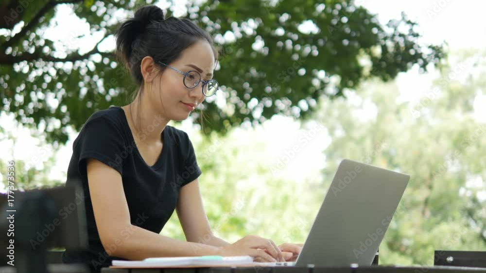 4K: Asian woman working on modern laptop in the park. 4K: Asian woman working on modern laptop in the park.