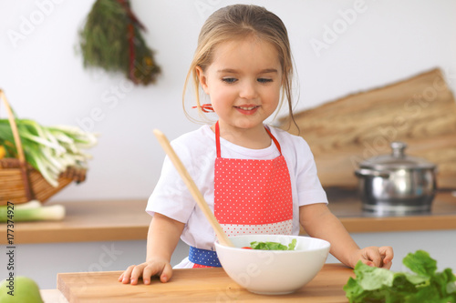 Little girl cooking in the kitchen. Kid slicing and mixing tomatoes and greenery. Concept of healthy meal or tasty breakfast