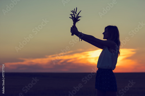 Beautiful woman holding wheat and enjoying the sunset in field.