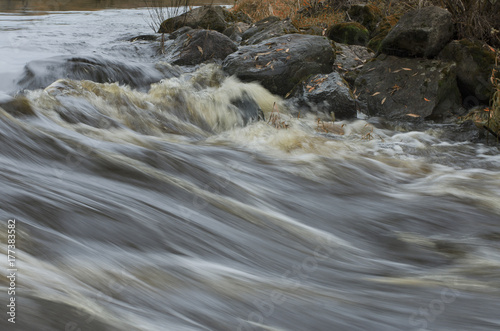 Rapid river flow and boulders with fallen leaves on the shore in autumn
