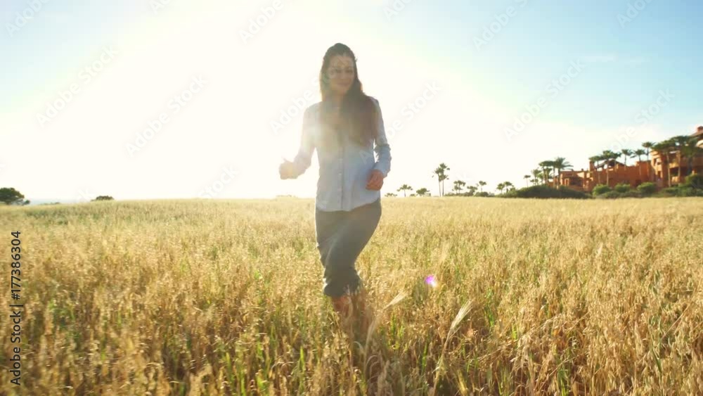 Beautiful girl walking and upping her arms in a wheat field with the sun behind Beautiful girl walking and upping her arms in a wheat field with the sun behind