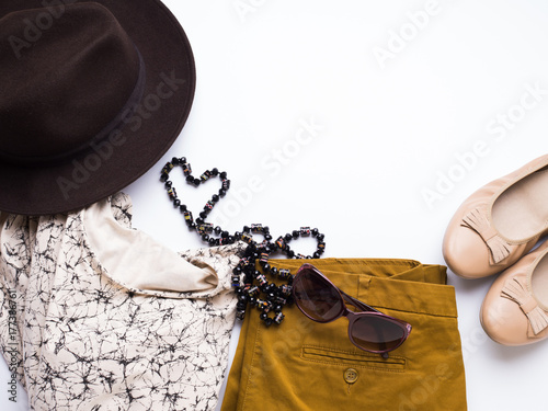 Flat lay with lady's clothes, hat, sun glasses, necklace. Autumn colours accessories on white background