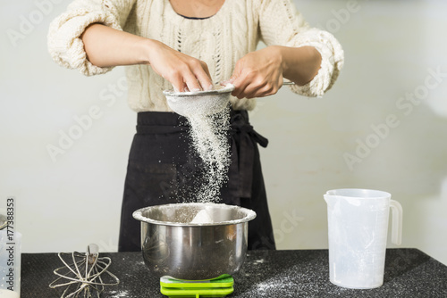 Young woman hands sifting flour into bowl for making batter. photo